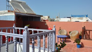 A rooftop terrace with a white balustrade, red chairs, wicker furniture, and potted plants. - Apparently familial  (Ancien Médina)