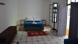 A bedroom with a bed, a bench, a window with a view, and a door. - Apparently familial  (Ancien Médina)