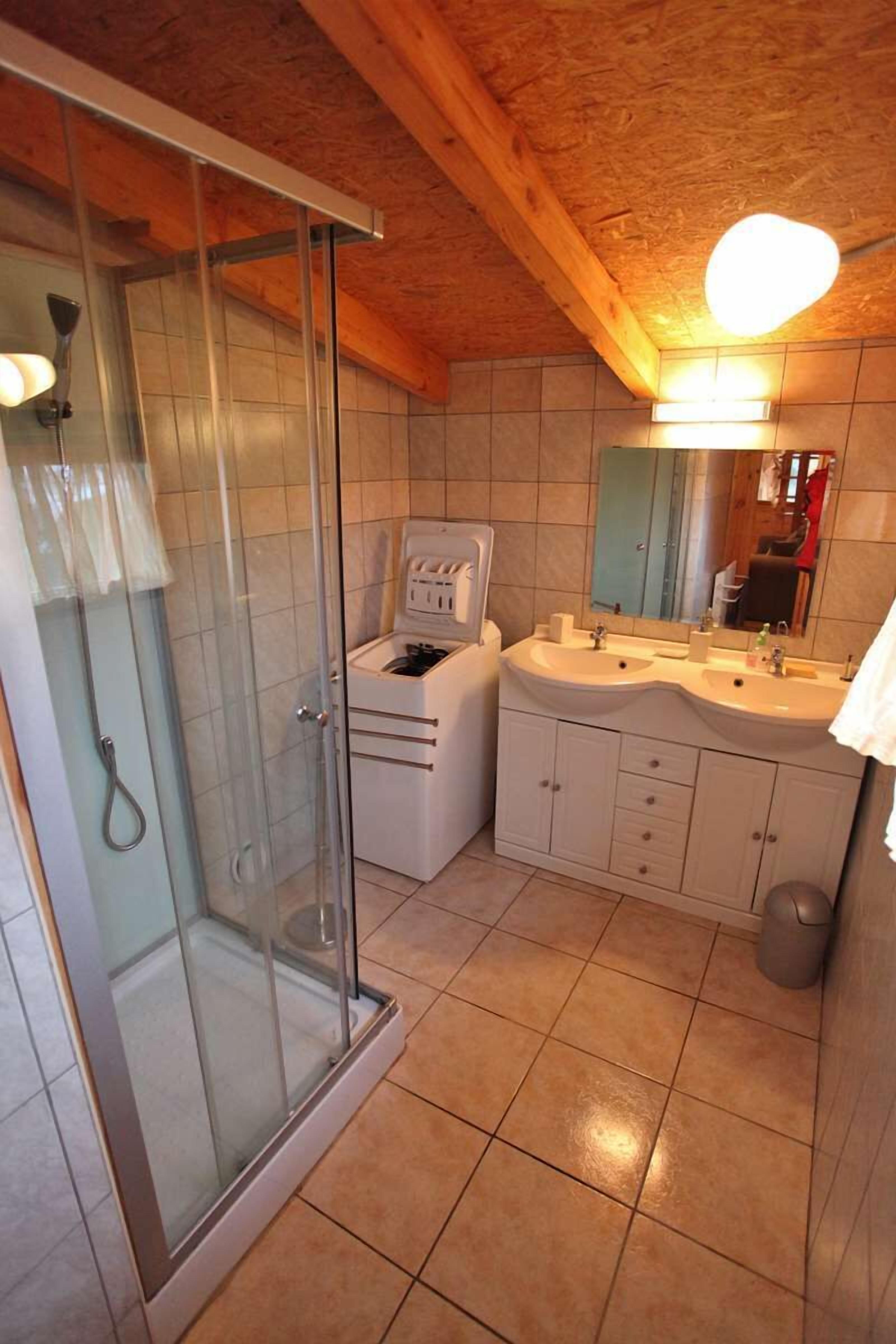 Un baño con cabina de ducha de vidrio, tocador blanco y espejo sobre el lavabo.