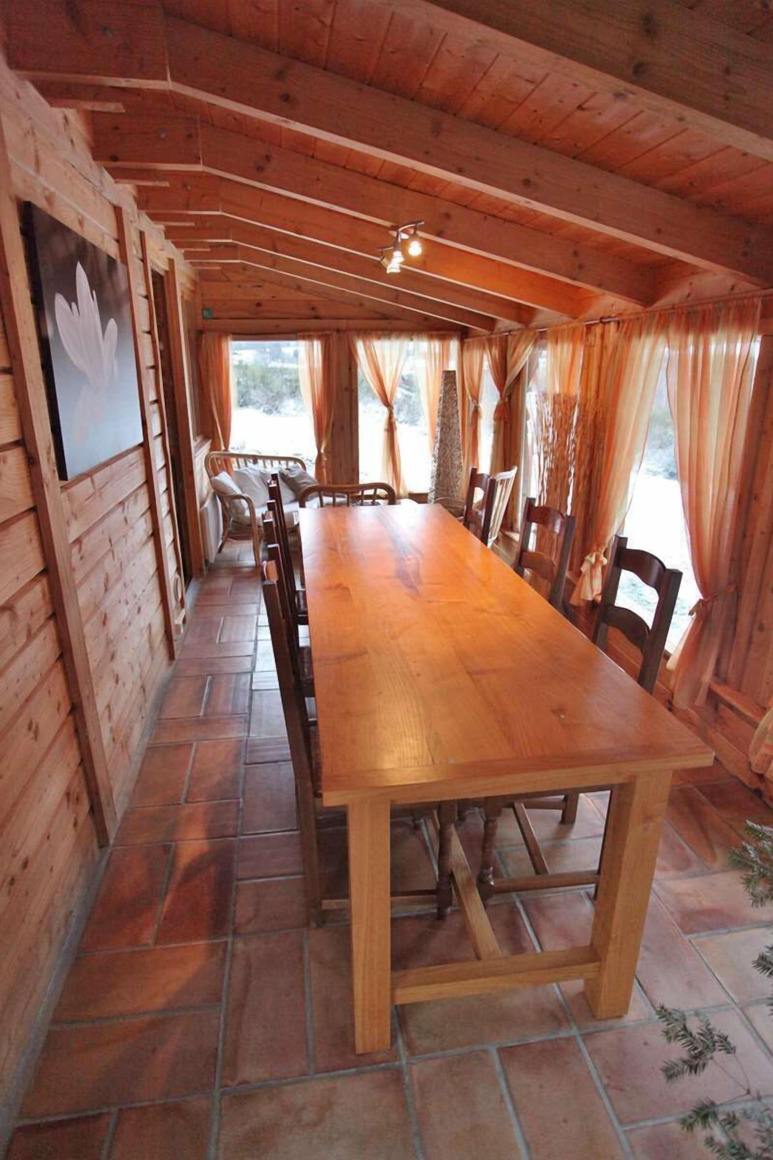 A wooden interior with a long dining table, chairs, and a fireplace.