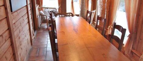 A wooden interior with a long dining table, chairs, and a fireplace.
