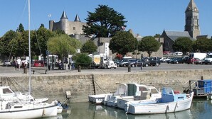 A harbor with several boats docked, a stone wall, and a church with a tall tower in the background.