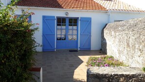 A white building with a red-tiled roof, a blue door with shutters, and a stone wall.