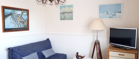 A room with a bed, a desk with a computer, a lamp, a chair, a small table with a duck figurine, and wall art.