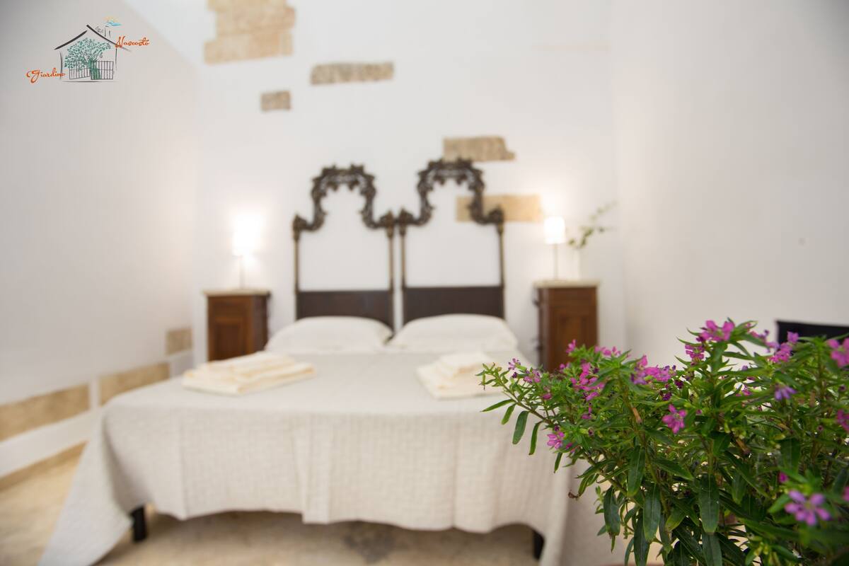Un dormitorio con cama, mesitas de noche y una lámpara fijada a la pared.