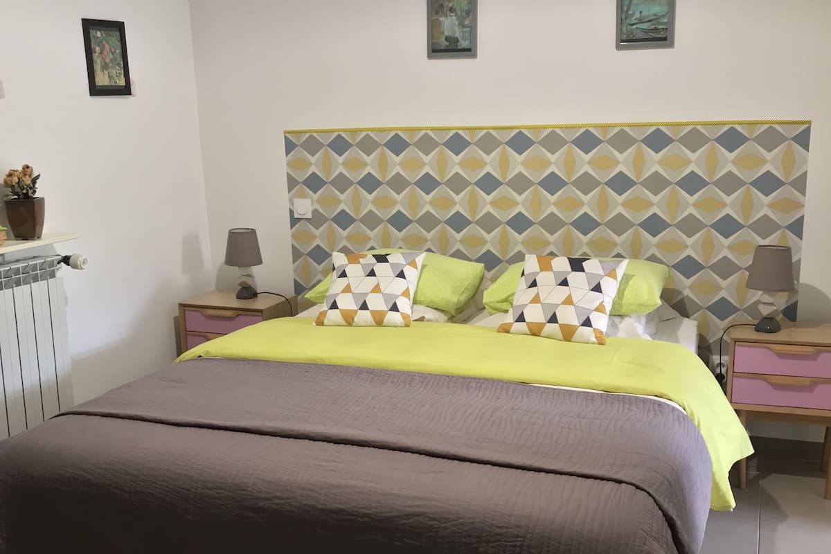 Un dormitorio con una cama, dos mesitas de noche, un radiador y una pared decorada con marcos.
