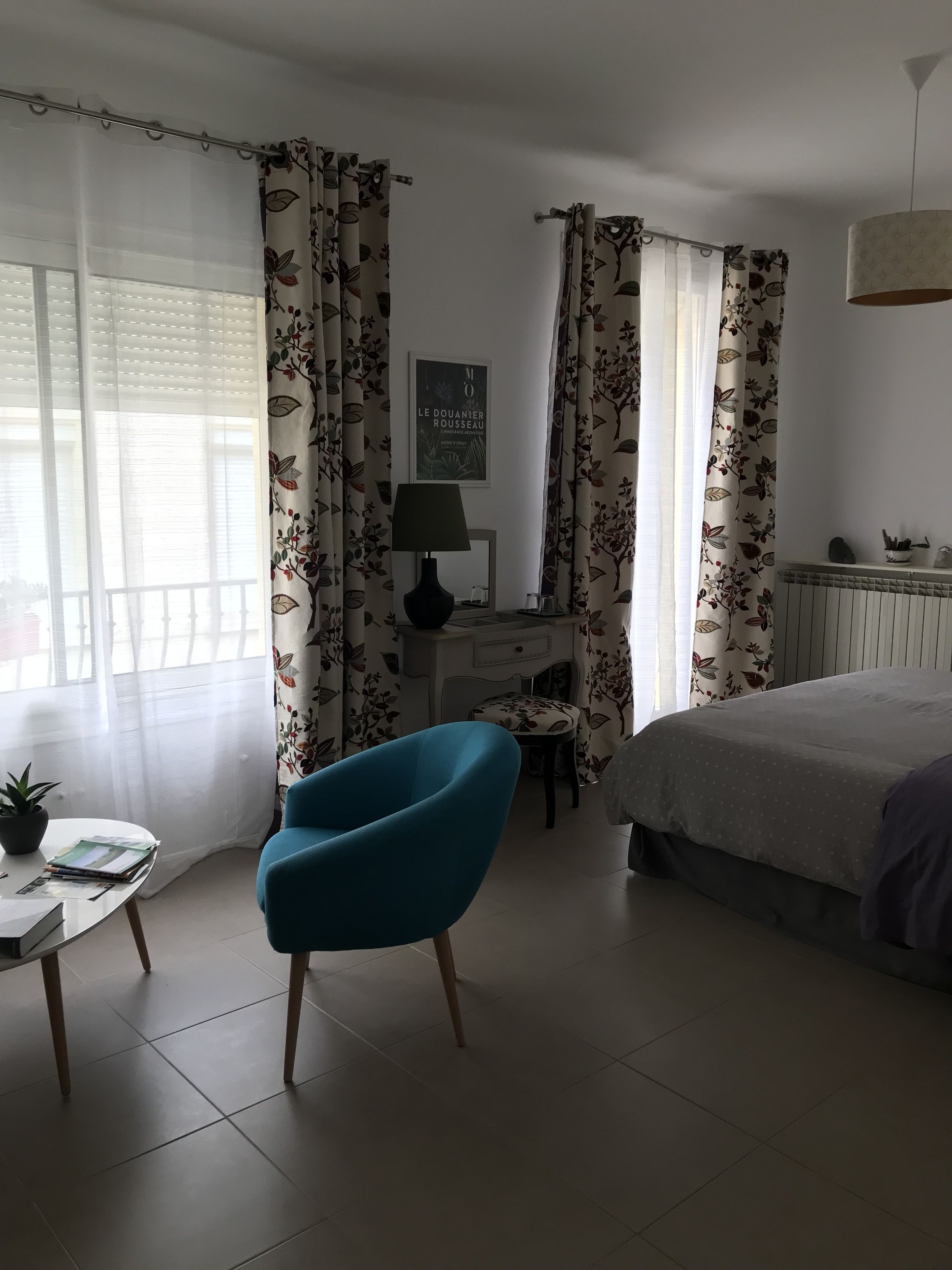 Un dormitorio con una cama, un escritorio con lámpara, una silla y cortinas con estampado floral.