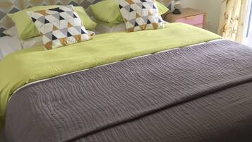 Een bed met een hoofdbord met een patroon, groene beddengoed en twee kussens met geometrische motieven.