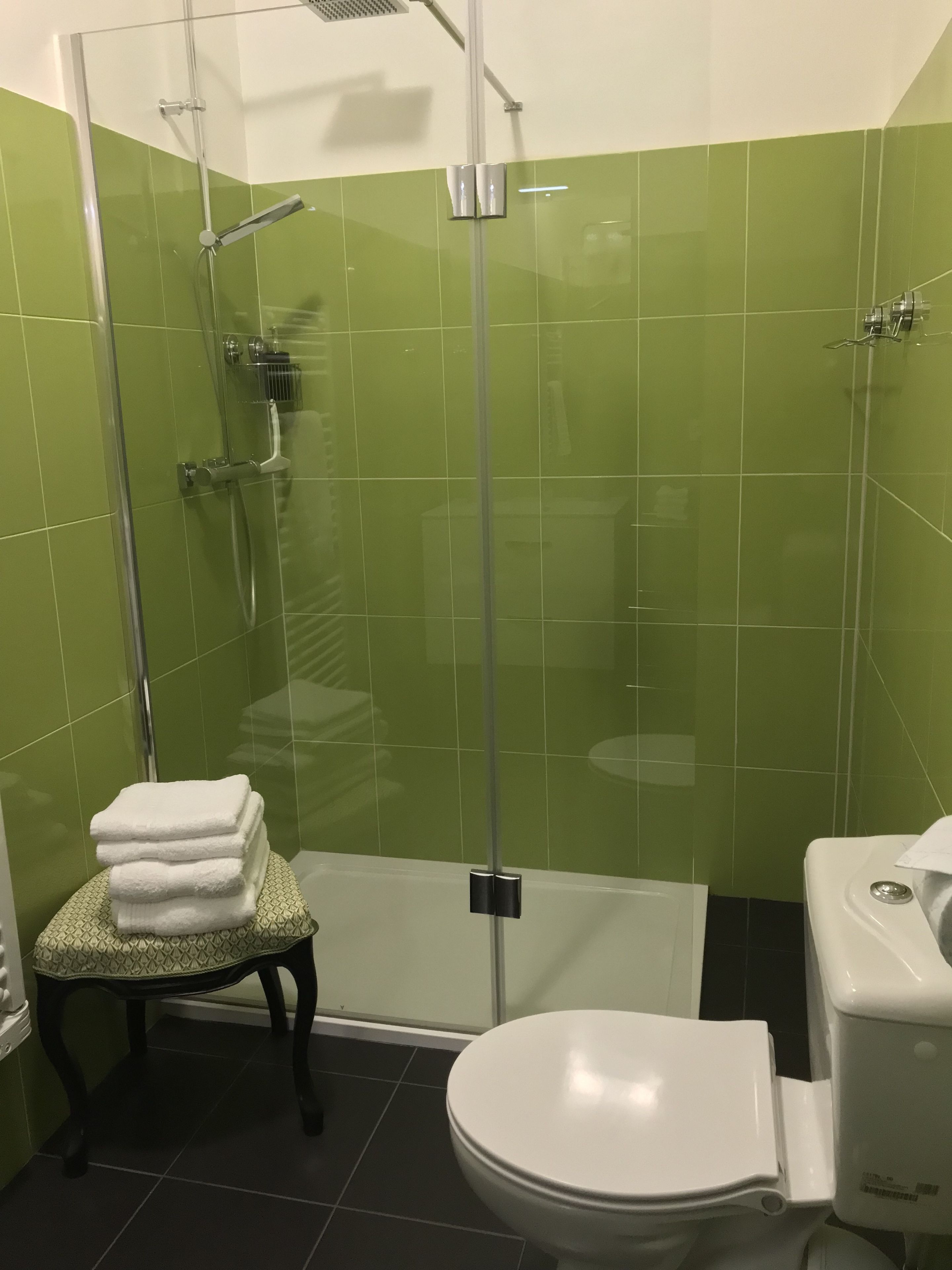 A bathroom with a glass-enclosed shower, a toilet, and a small table with towels.