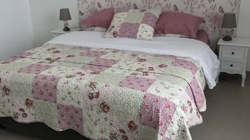 A neatly made bed with a floral quilt, a white headboard with a butterfly pattern, and a bedside table with a lamp.
