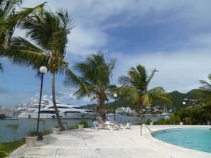 A poolside area with lounge chairs, palm trees, and a yacht in the background.