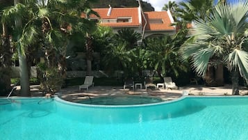 En swimmingpool omgivet af palmer og et hus med rødt tegltag.