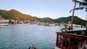 A coastal view with a wooden railing, a palm tree, and a distant town by the sea. - Sint Maarten 2 Bedrooms Simpson Bay (Simpson Bay)