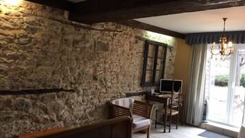 A rustic room with a stone wall, a wooden bench, a small table with chairs, and a window with curtains.