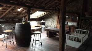 A rustic attic room with exposed wooden beams, stone walls, and a skylight. There are two wooden stools and a bench. - Chambres d'Hôtes les Hirondelles (Folkling)