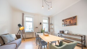 Ein modernes Wohnzimmer mit einer Couch, einem Esstisch, Stühlen, einer Stehlampe und einem Bild an der Wand.