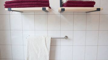 A bathroom with white tiled walls, two towel racks with folded towels, and a metal towel rack with a single towel.