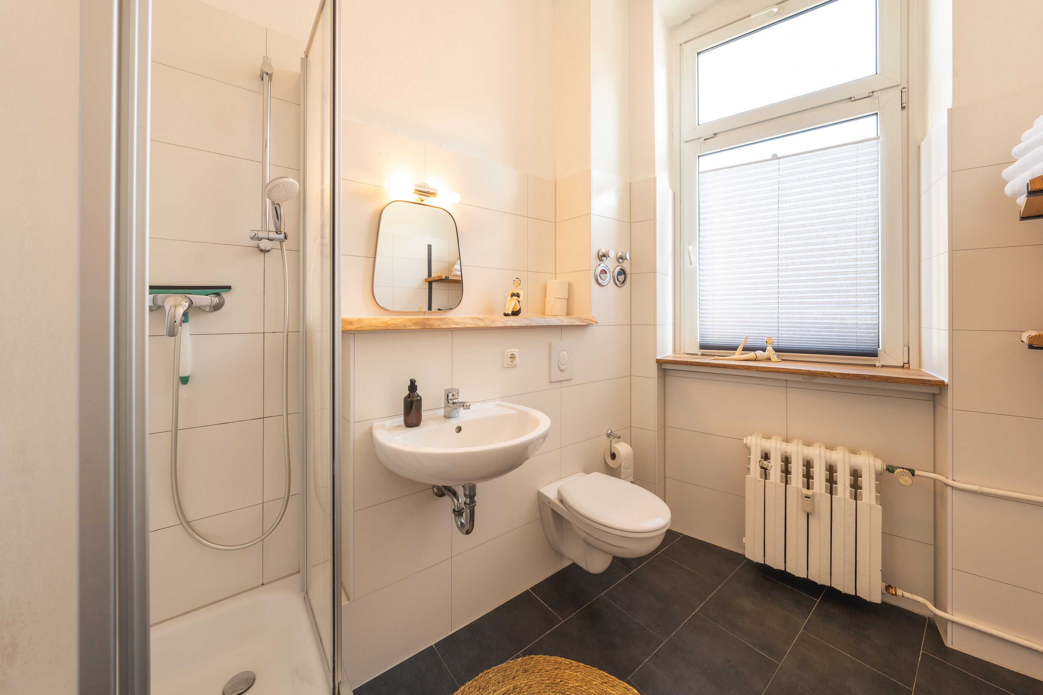 Un ba ño con cabina de ducha de vidrio, un lavabo blanco, un inodoro y un radiador.