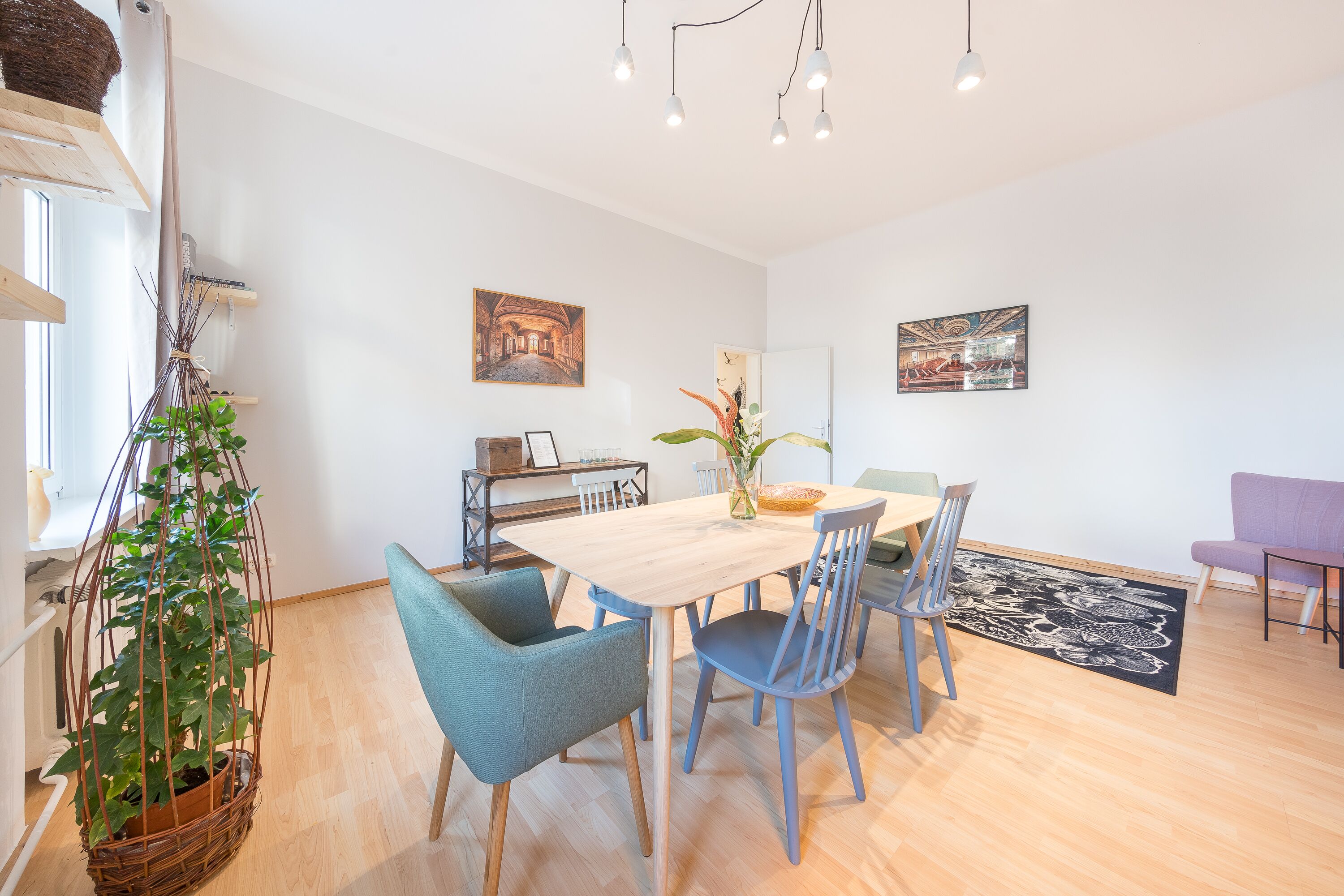 Un coin repas avec une table en bois, des chaises bleues et une plante suspendue.