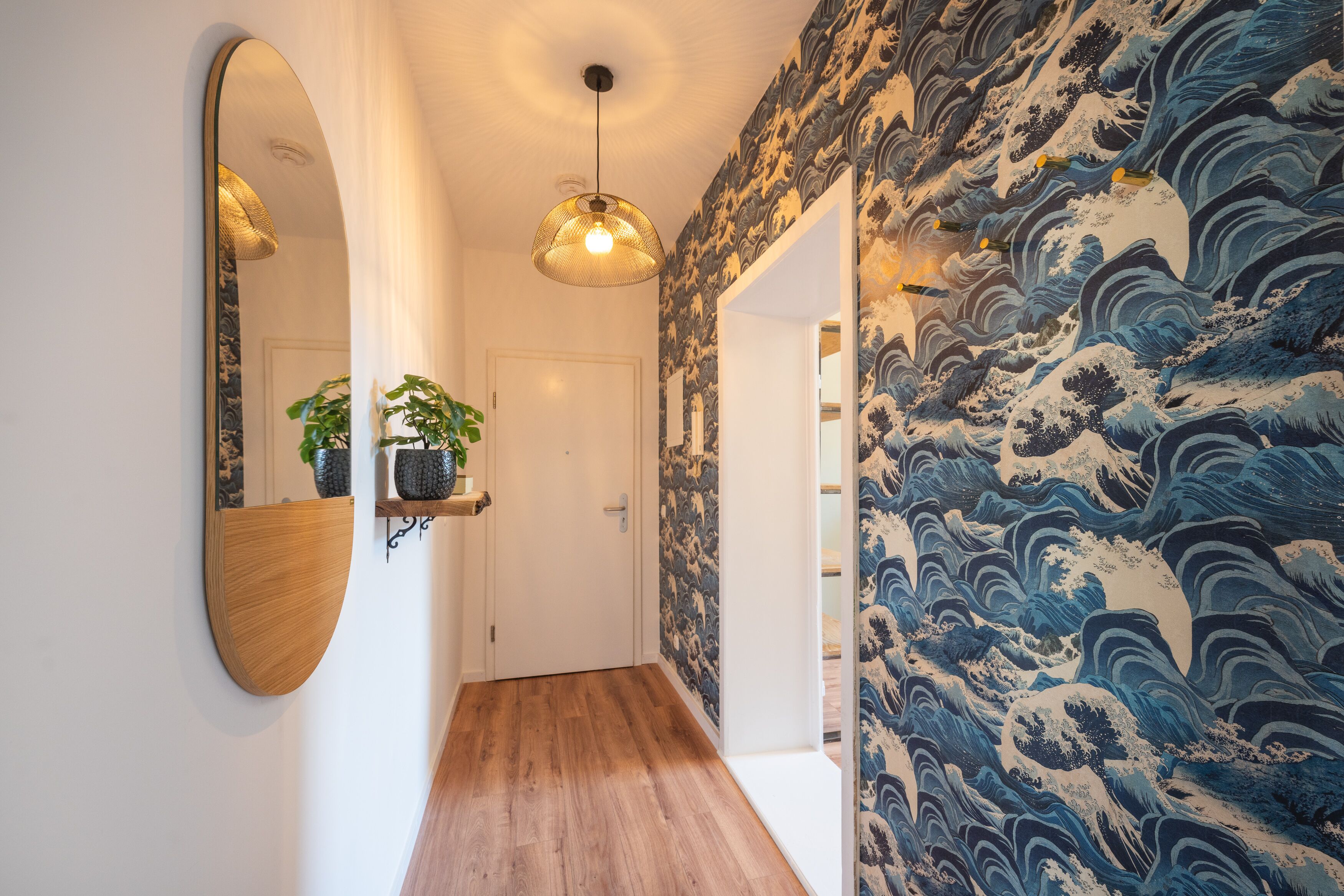 A hallway with a wooden floor, a round mirror, and a hanging light fixture.