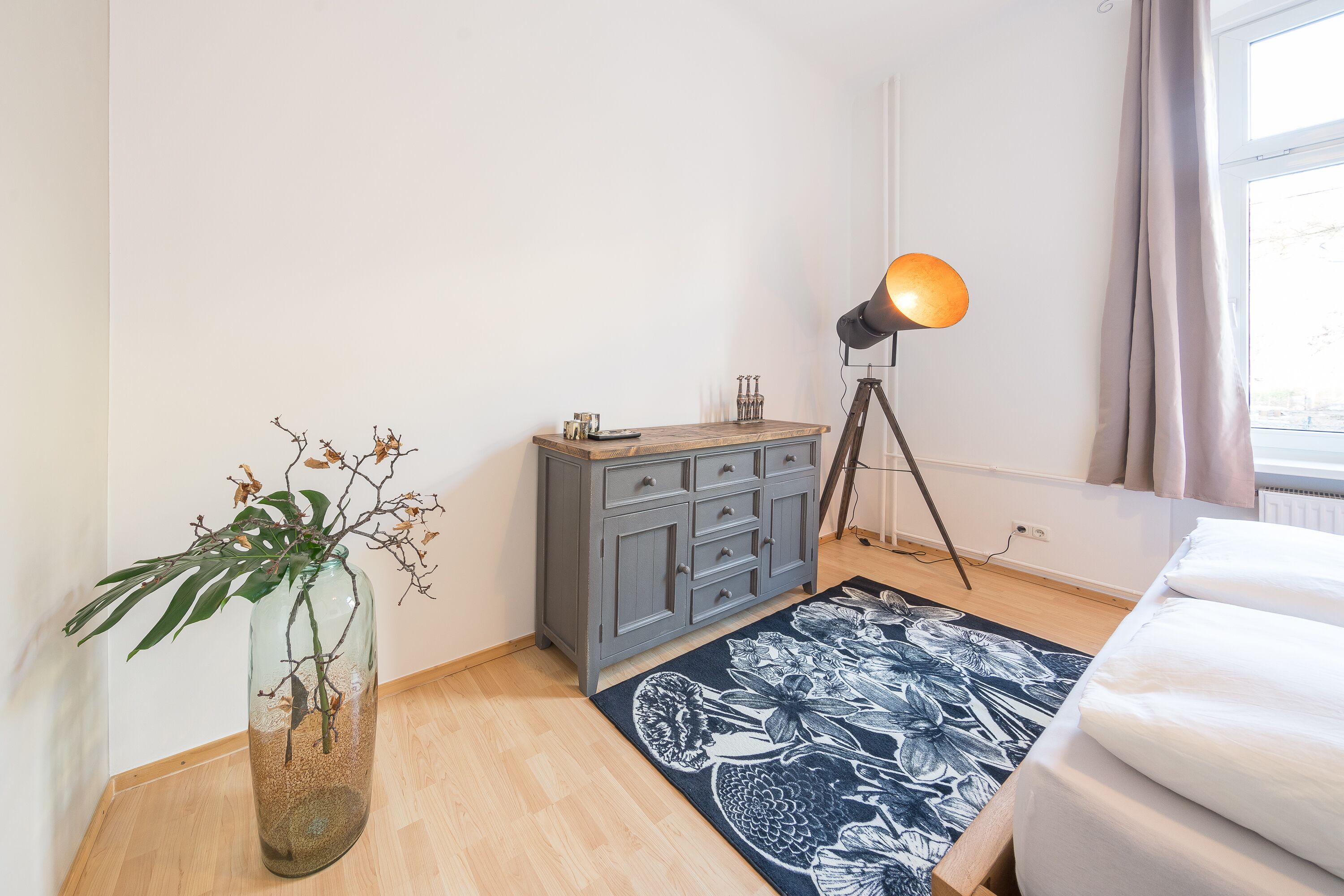 A bedroom with a bed, a dresser, a lamp, and a vase with a plant.