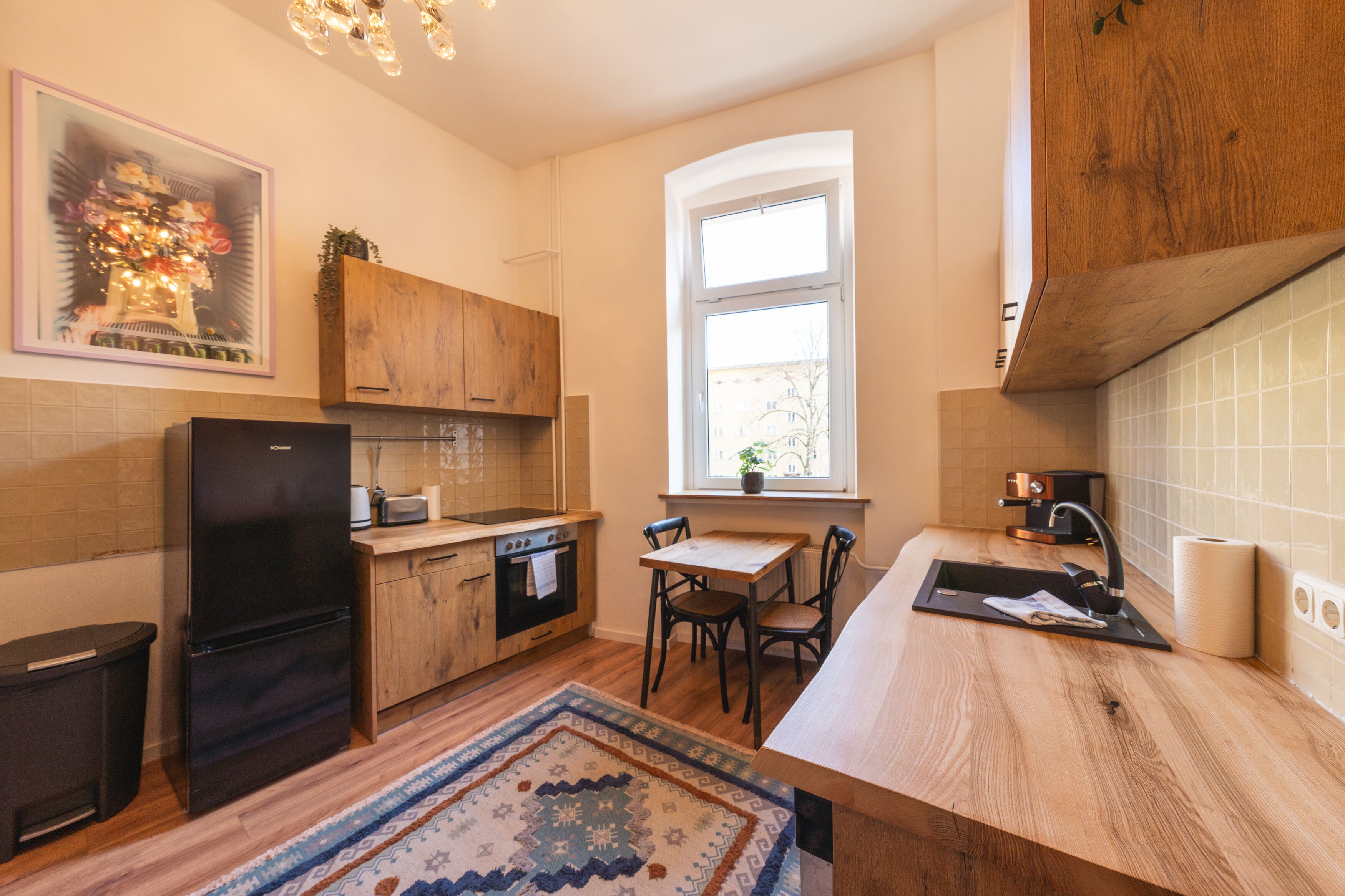 Una cucina moderna con mobili in legno, un frigorifero nero, un tavolo da pranzo con sedie, una finestra con vista e un tappeto decorato.