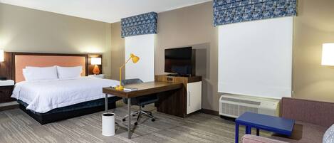 A hotel room with a bed, desk, chair, and a television.
