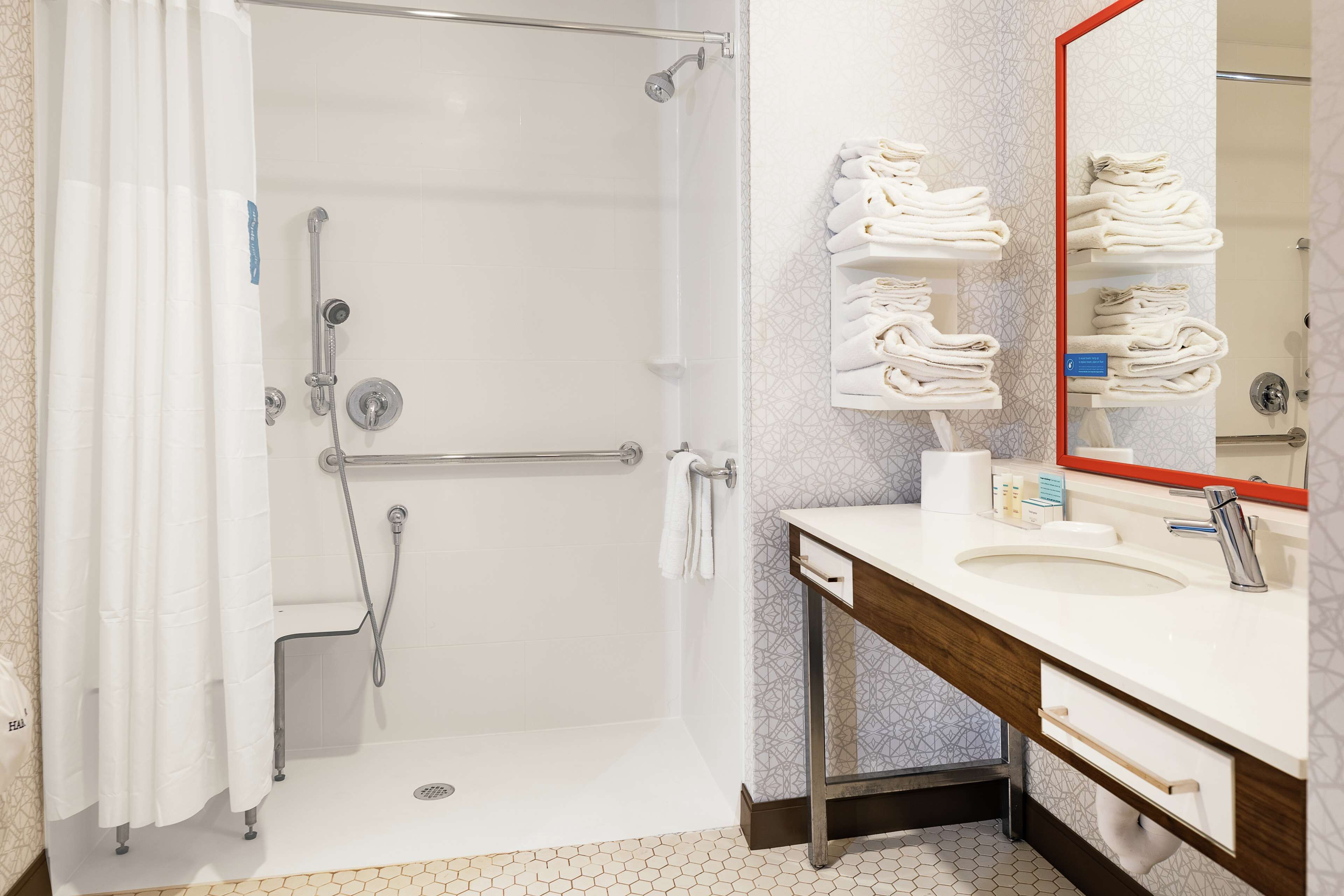 A bathroom with a shower, a sink, a mirror, and a towel rack.
