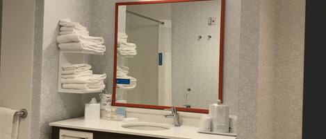 A modern bathroom with a white sink, a mirror with a red frame, and a towel rack with folded towels.