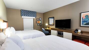 A hotel room with two beds, a desk with a computer, a TV, and a window with blinds.