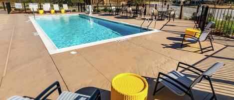 A swimming pool with lounge chairs and umbrellas, surrounded by a fenced area with a clear sky.