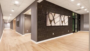 Un pasillo moderno de hotel con suelo de madera, paredes de ladrillo oscuro y una gran obra de arte abstracta.