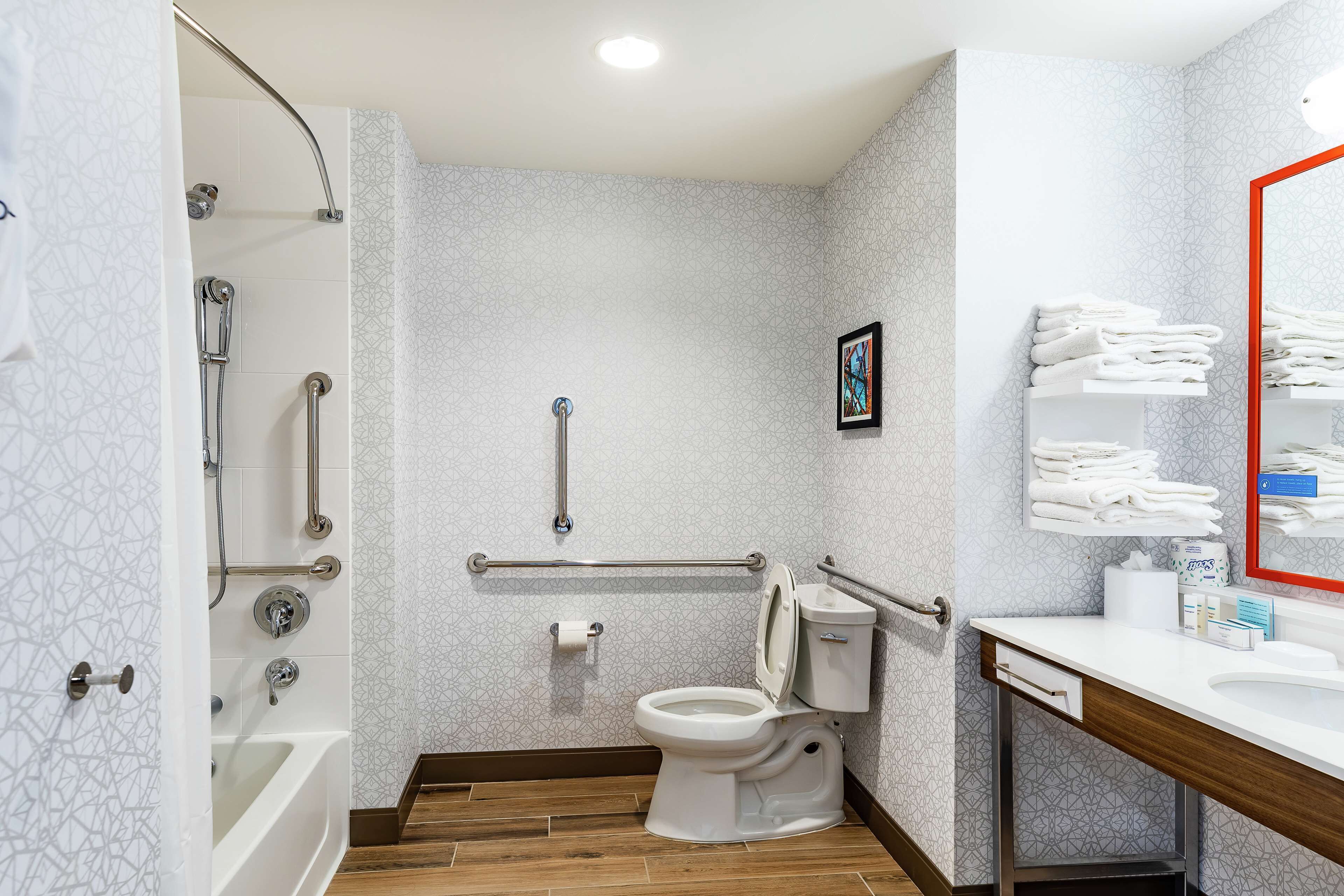 Un baño con ducha, inodoro y lavamanos, equipado con barras de apoyo y un pasamanos.