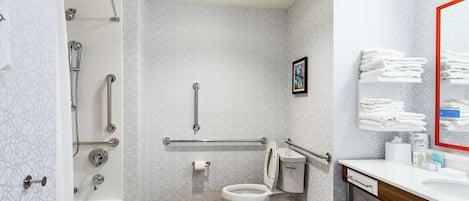 Een badkamer met douche, toilet en wastafel, voorzien van handgrepen en een handrailing.