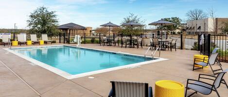 A pool area with lounge chairs, umbrellas, and a clear sky.