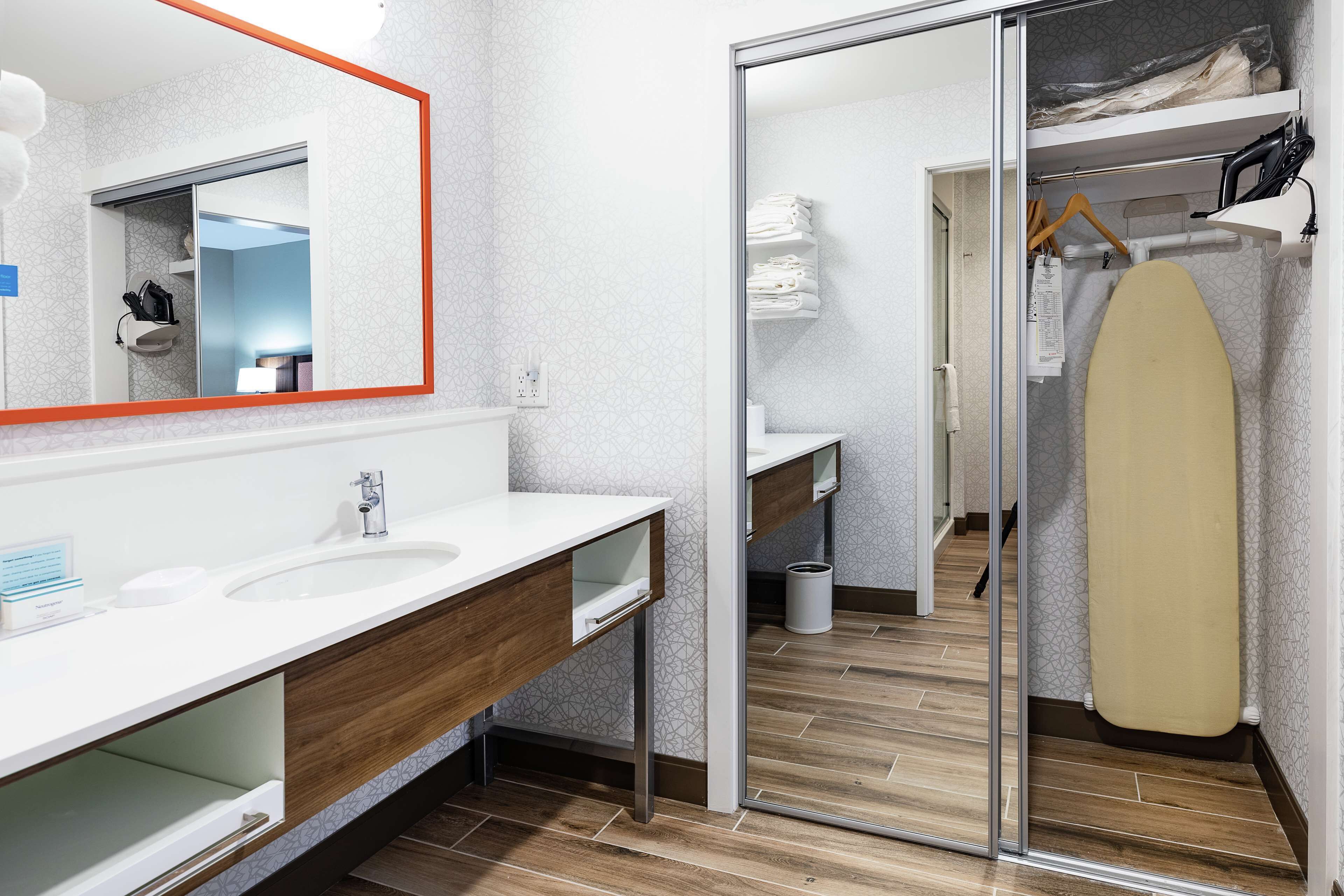 Een moderne badkamer met een wit wastafelmeubel, houten opbergruimte en een grote spiegel.