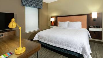 A hotel room with a bed, a desk with a lamp, a television, and a window with a view.