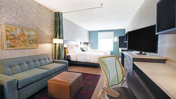 A hotel room with a sofa, a bed, a desk, a TV, and a painting on the wall.
