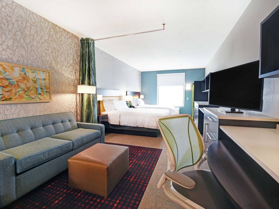 A hotel room with a sofa, a bed, a desk, a TV, and a painting on the wall.