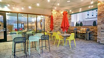 An outdoor patio area with tables and chairs, a barbecue grill, and string lights.
