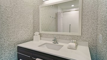 Un baño con lavamanos blanco, tocador de madera oscura y un espejo grande.