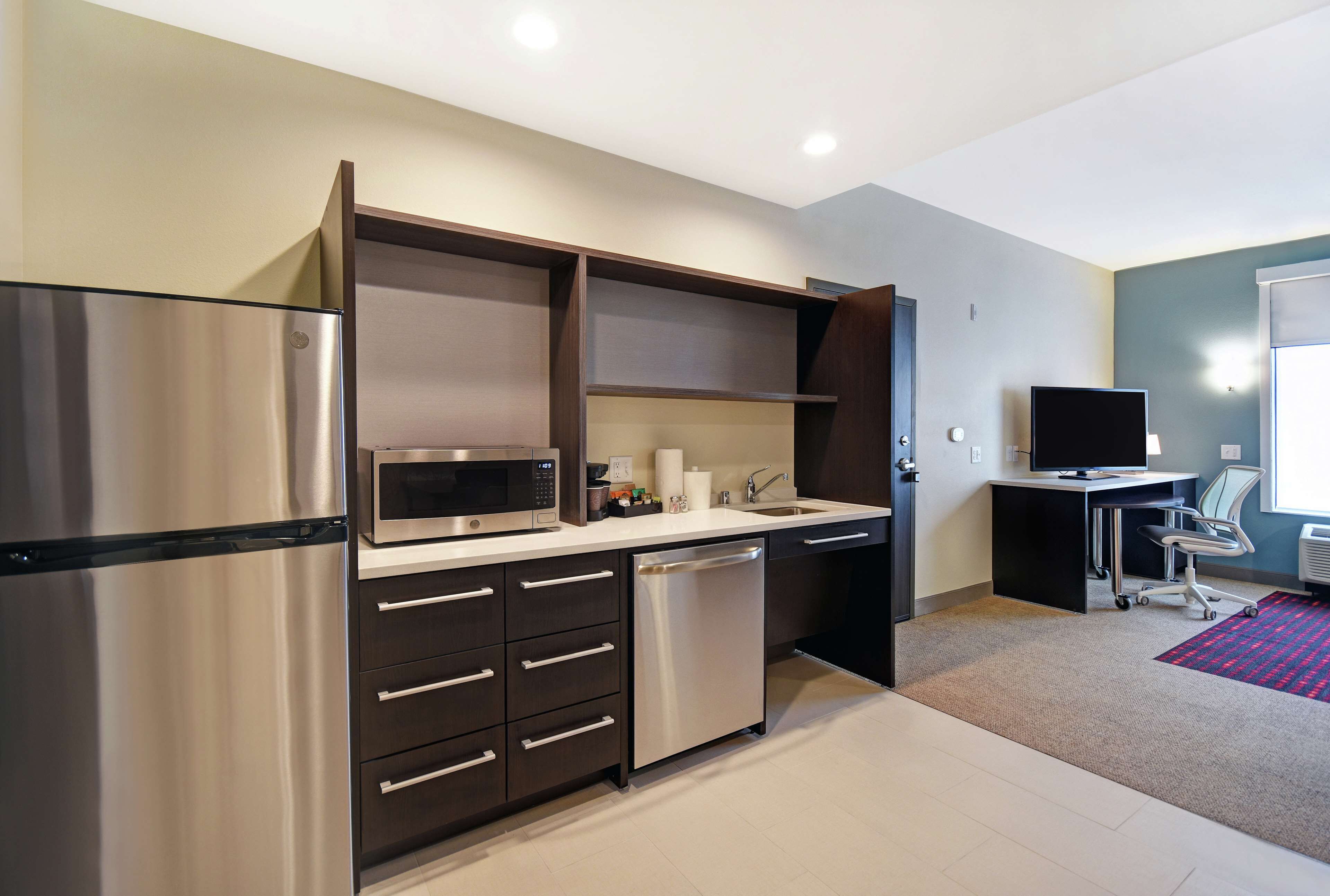 A modern kitchen with a stainless steel refrigerator, microwave, and dishwasher, a sink, and a small desk with a chair.