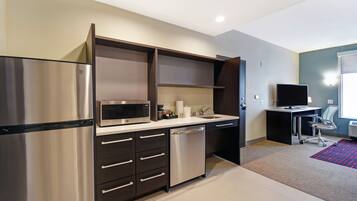 A modern kitchen with a stainless steel refrigerator, microwave, and dishwasher, a sink, and a small desk with a chair.
