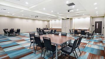 A conference room with a large table and multiple chairs, carpeted floor, and a projector screen.