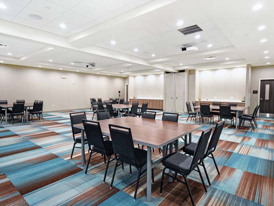 A conference room with a large table and multiple chairs, carpeted floor, and a projector screen.