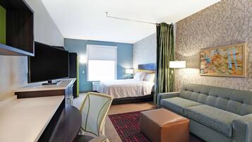 A hotel room with a bed, a desk, a chair, a sofa, and a painting on the wall.