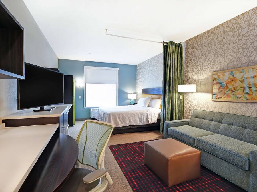 A hotel room with a bed, a desk, a chair, a sofa, and a painting on the wall.
