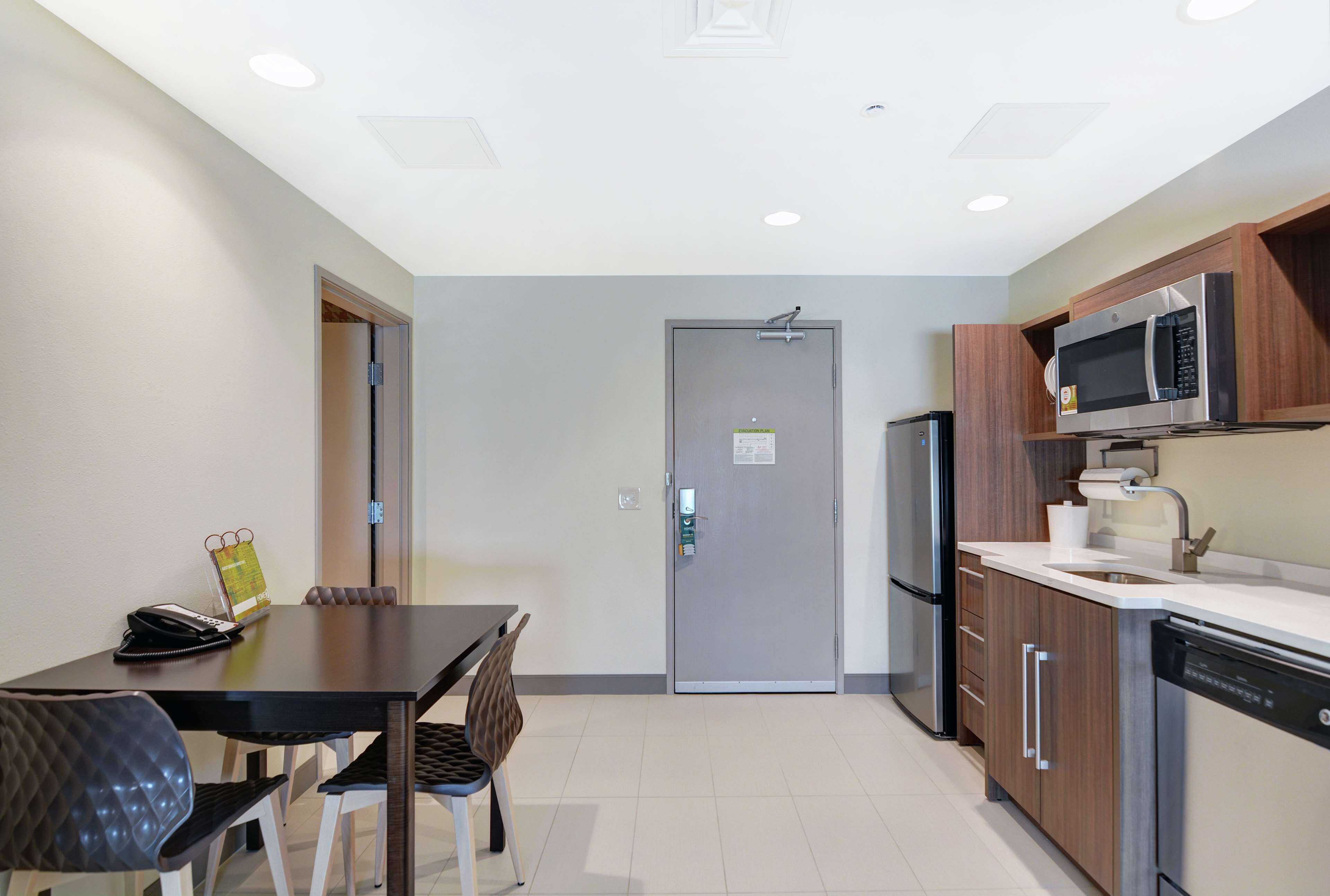 Cocina compacta equipada con refrigerador, microondas y lavavajillas. Hay una mesa de comedor con sillas y una puerta que da a otra habitación.