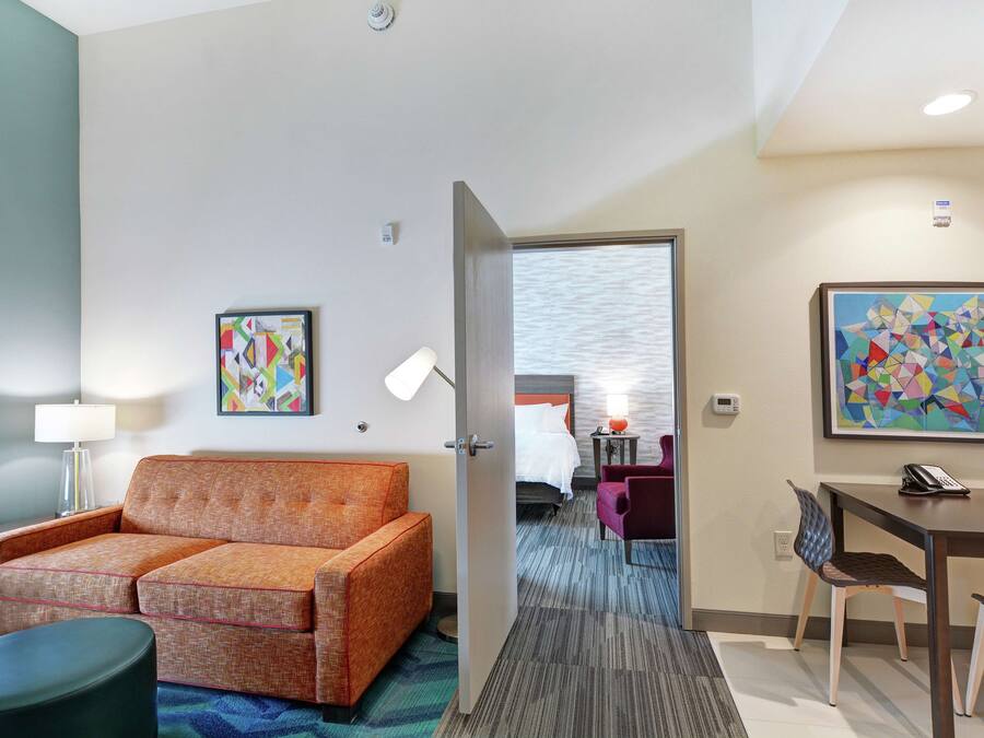 Une chambre d’hôtel équipée d’un canapé, d’une table à manger, d’une chaise, d’une lampe et d’un lit avec une table de chevet.