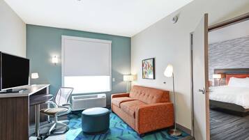 A hotel room with a desk, chair, sofa, ottoman, and a bed.
